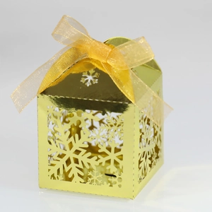 Détail de la boîte cadeau dorée en forme de maison avec flocons découpés et ruban