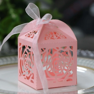 Detail of pink laser-cut rose hollow candy box with translucent ribbon on white plate
