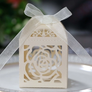 Detail of cream laser-cut rose paper candy box with white organza ribbon bow on a plate