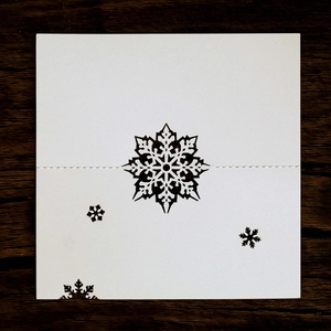 Detail of laser-cut snowflake hollow on white place card over wooden background