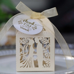 Detail of laser-cut ivory wedding favor box with ribbon and thank you tag on a white plate