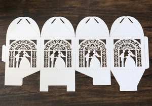 Flat lay of laser-cut white wedding candy box template with bride and groom silhouette