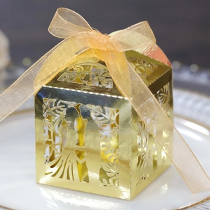 Detailed view of golden laser-cut wedding favor box with ribbon on a white plate