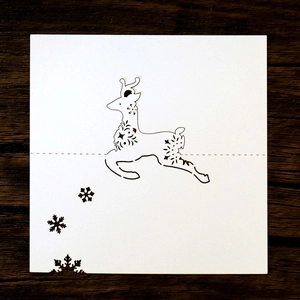 Detail of laser-cut white stag and snowflake place card on vintage wood background