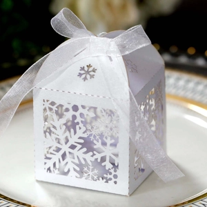 Detail of white laser-cut snowflake hollow gift box with elegant ribbon on porcelain plate