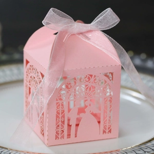 Close-up of pink laser-cut wedding favor box with bride and groom silhouette and ribbon