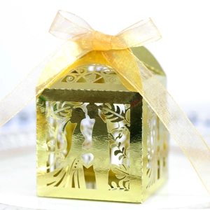 Macro view of gold laser-cut wedding candy box with heart pattern and silk ribbon