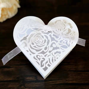 Detail of laser-cut rose patterns on a white heart-shaped wedding favor box with ribbon