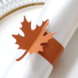 Macro shot of maple leaf napkin ring in caramel orange on a gold-rimmed white porcelain plate