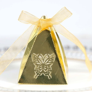 Macro detail of golden pyramid candy box featuring laser-cut butterfly and silk ribbon
