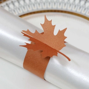 Detailed macro shot of a laser-cut red maple leaf napkin ring on a white satin cloth