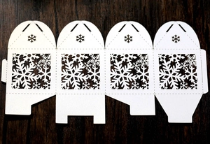 Flat lay of white laser-cut snowflake hollow candy box template on dark wood background
