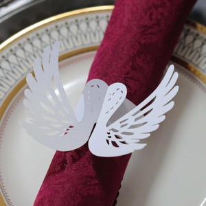 Macro shot of white swan paper napkin ring with heart cutout on a burgundy fabric