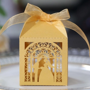 Close-up of golden laser-cut wedding candy box with bride and groom silhouette and ribbon