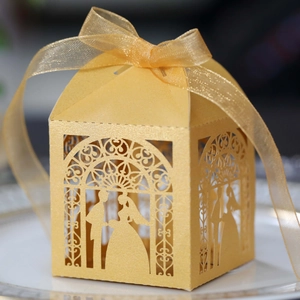 Detail of laser-cut gold wedding candy box with bride and groom silhouette and ribbon