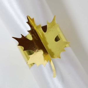 Macro shot of gold maple leaf napkin ring with detailed metallic veins on white silk