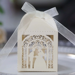 Detail of laser-cut cream wedding favor box featuring bride and groom silhouette with ribbon