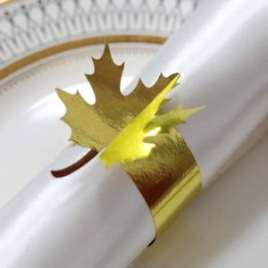Detailed view of a golden maple leaf napkin ring with polished finish on a white cloth