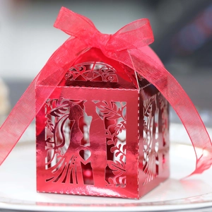 Macro detail of red laser-cut wedding candy box with bride and groom silhouette and ribbon