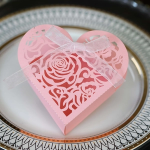 Pink heart-shaped laser-cut wedding favor box with rose patterns and ribbon detail