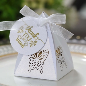 Detail of white pyramid favor box with golden butterfly cutout and Thank You tag
