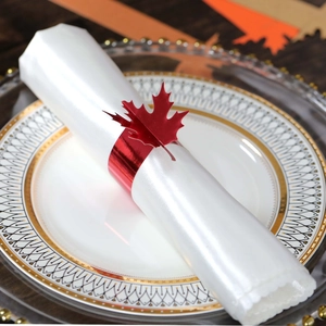 Detail of a red metallic maple leaf napkin ring on a white plate for festive table decor
