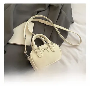 Detailed shot of cream mini bowling bag featuring a metallic bow and top handles