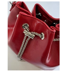 Detail of red patent leather bucket bag featuring silver drawstring chain and metal eyelets