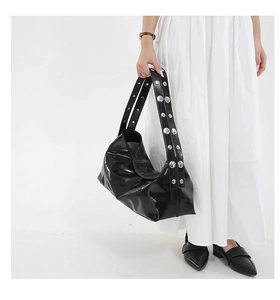 Detail of glossy black shoulder bag with silver metallic rivets on a wide strap