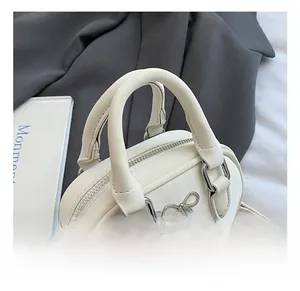 Close-up of white leather bowling bag with metallic bow detail and zip closure