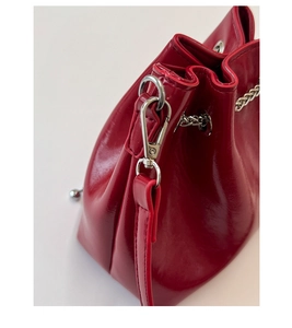 Detail of red patent leather bucket bag featuring silver metal chain and smooth stitching