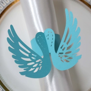 Detail of laser-cut blue swan napkin ring on white satin cloth and gold-rimmed plate