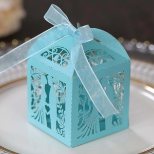 Detail of light blue laser-cut wedding candy box with silk ribbon on a plate