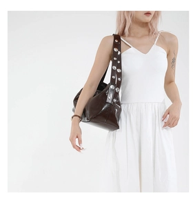 Detail of dark brown shoulder bag featuring shiny faux leather and silver metal rivets