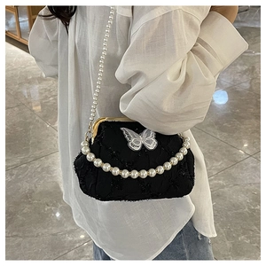 Detail of a black quilted bag featuring white butterfly decor and pearl handle straps