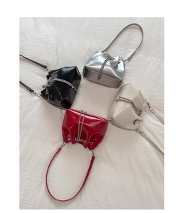 Overhead view of four glossy bucket bags in black, silver, beige, and red with chain straps