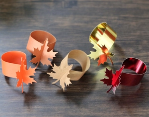 Close-up of maple leaf napkin rings in five metallic colors on dark wood background