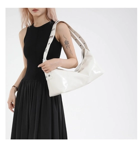 Detail of white patent leather hobo bag with large silver metal grommets on strap