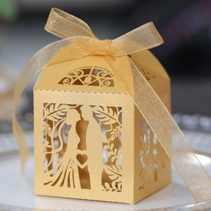 Close-up of golden laser-cut wedding candy box with leaf pattern and silk ribbon bow