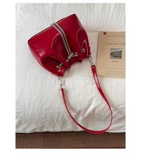 Vue détaillée du sac seau en cuir rouge avec chaîne argentée sur tissu texturé blanc