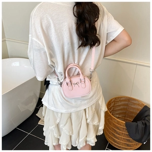 Pink mini bowling bag with silver bow accent worn as a crossbody in a modern setting
