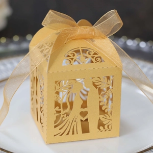 Detail of gold laser-cut wedding candy box with bride and groom silhouette and ribbon bow
