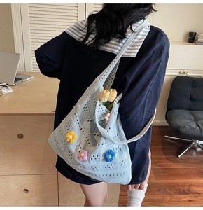 Detail of light blue knit tote bag featuring colorful 3D floral crochet accents