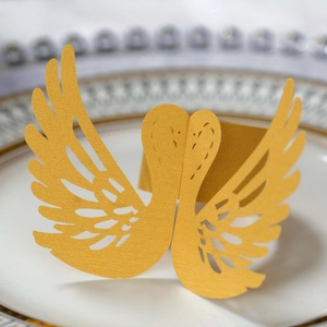 Detailed laser-cut golden swan napkin ring with intricate hollow wing patterns on white plate