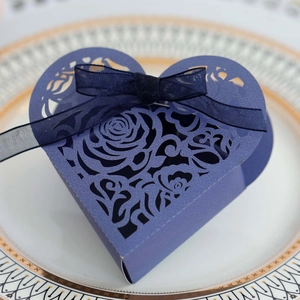 Macro detail of laser-cut rose patterns on a heart-shaped wedding candy box with ribbon