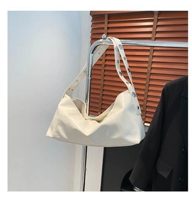 Detail of off-white hobo bag with wide strap and silver metal rivets on a hanger