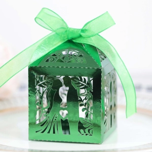 Detailed laser-cut hollow green wedding favor box with ribbon on a porcelain plate
