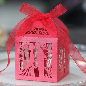 Detail of red hollow laser-cut wedding favor box with ribbon on a white ceramic plate