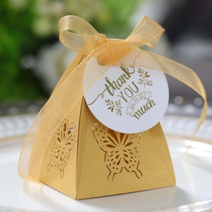 Detailed laser-cut butterfly on golden pyramid gift box with ribbon and thank you tag