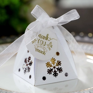 Close-up van wit geschenkdoosje met gouden sneeuwvlokken, bedanklabel en zijden lint